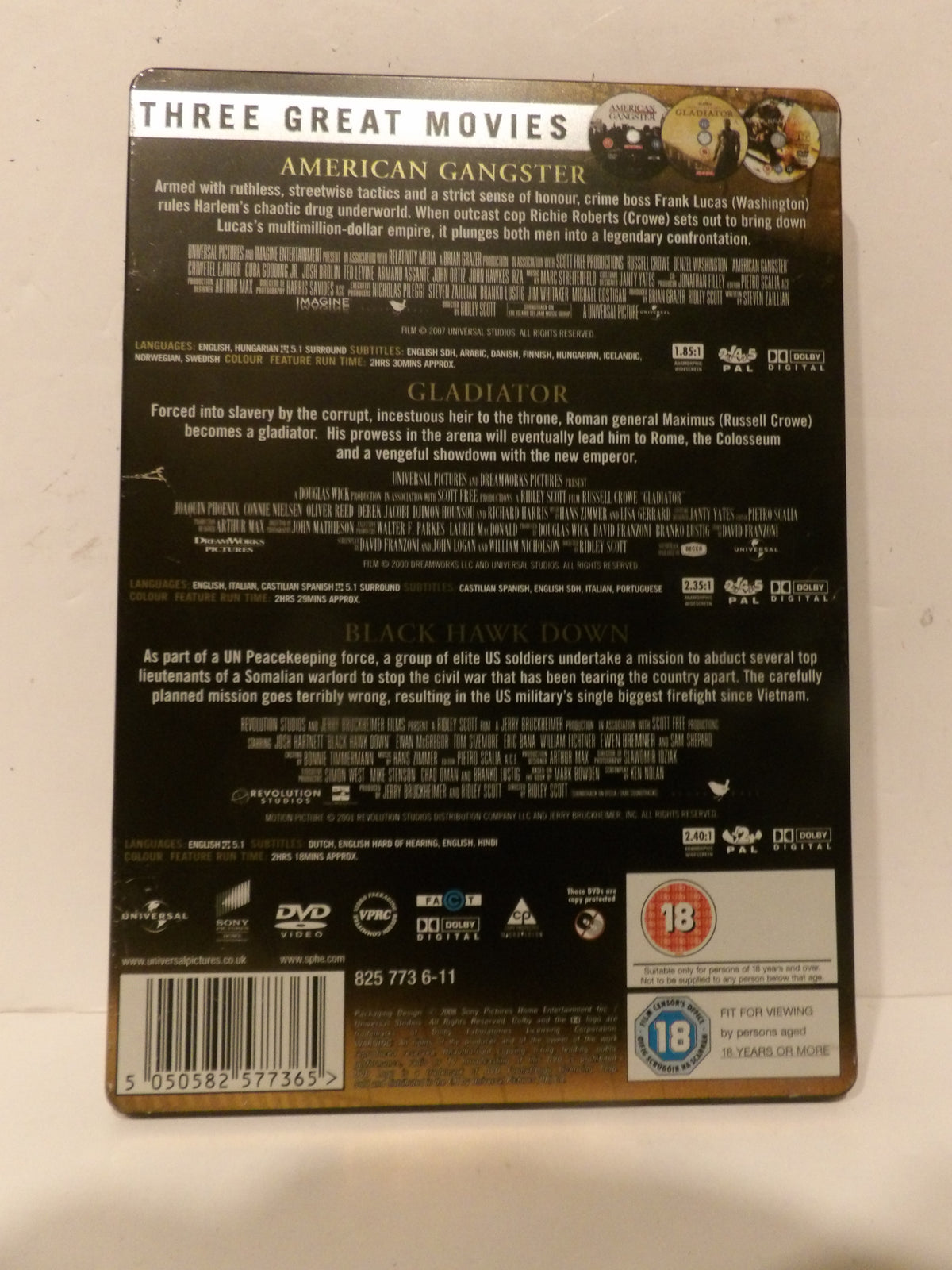 The back cover of a DVD box set for 'Three Great Movies' featuring films American Gangster, Gladiator, and Black Hawk Down, with extensive credits on a black background and a gold border.
