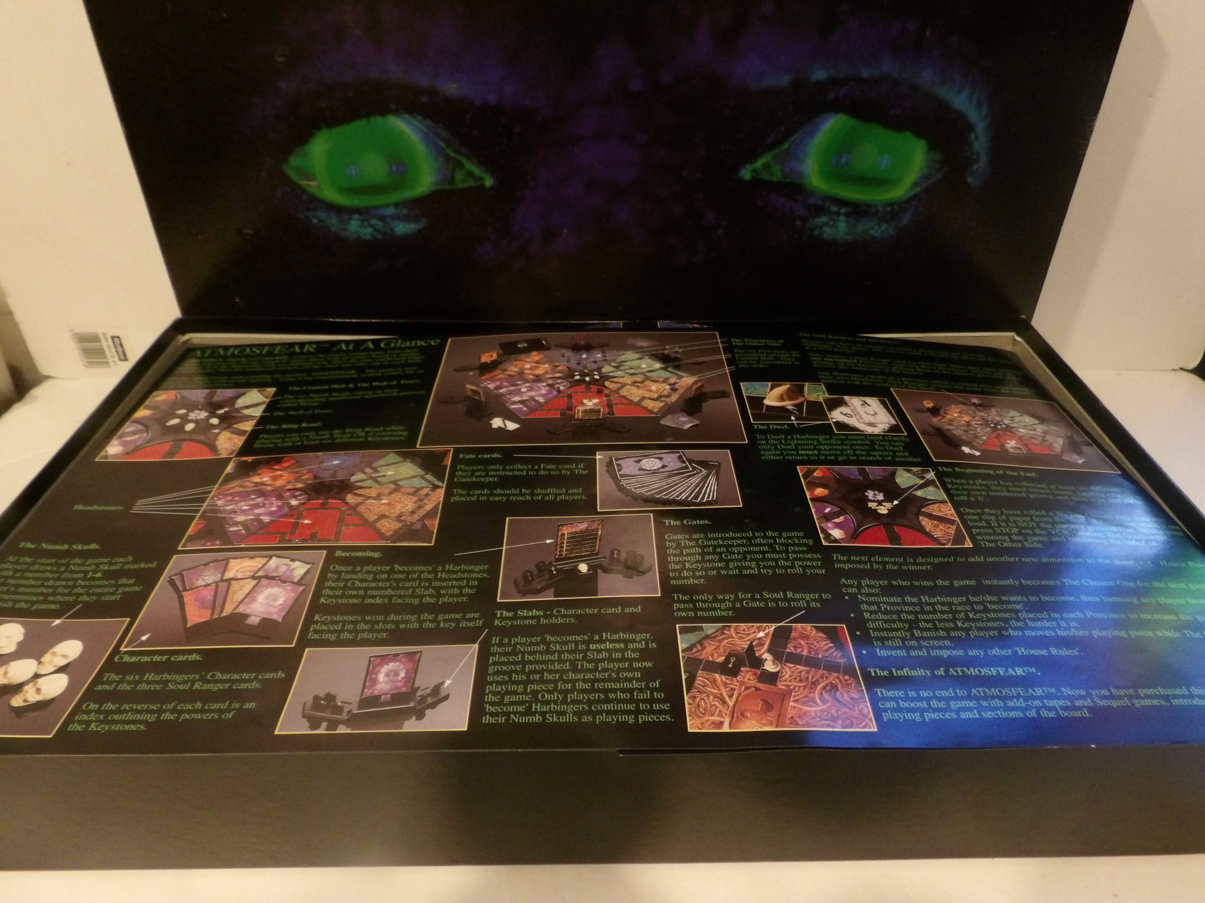 A vintage tabletop gaming display case, likely for GURPS, featuring a black interior with printed rules text, character cards, and illustrations, and a matching black backdrop panel with glowing green eyes.