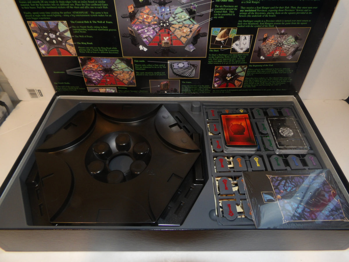 Open Magic: The Gathering trading card game box showing the black game board, black components, a red-orange card, and multiple card packs inside the tray, with the inner lid displaying game artwork and rules text.