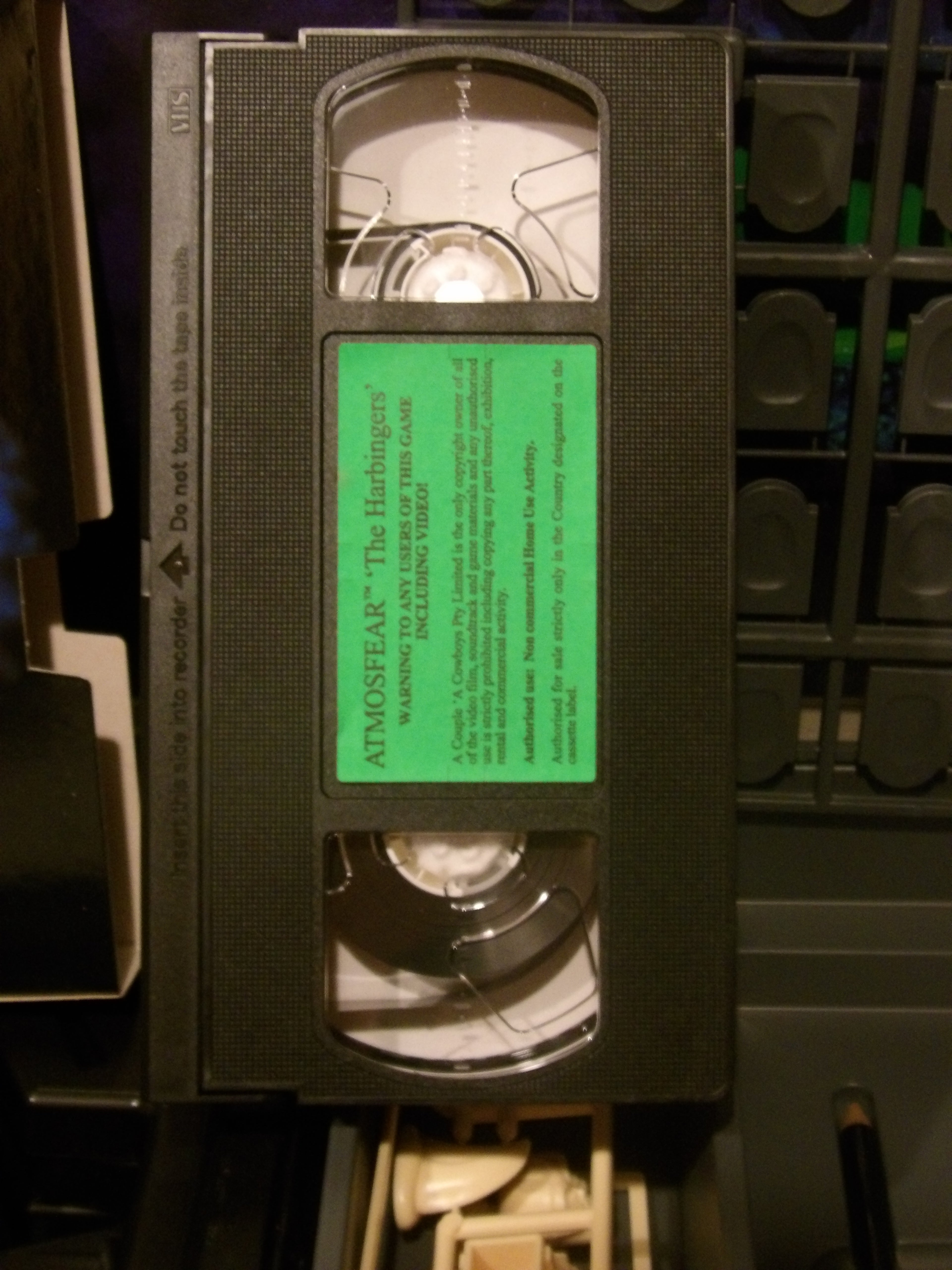 A VHS tape of the movie 'Atmospheric' with a bright green label, photographed inside a dark storage bin.