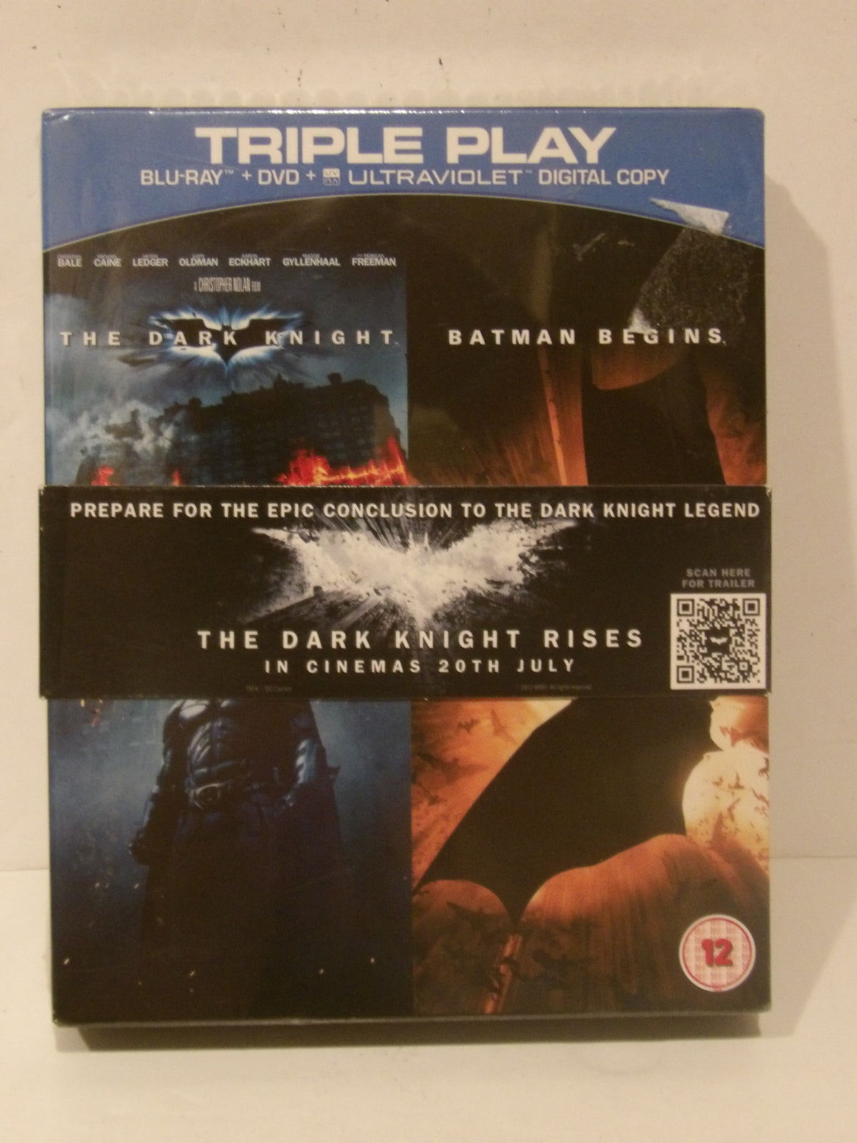 A boxed movie bundle for The Dark Knight Trilogy, featuring The Dark Knight, Batman Begins, and The Dark Knight Rises on a single cover with blue, black, and fiery orange artwork. Text at the top reads 'TRIPLE PLAY' and 'BLURAY + DVD + ULTRAVIOLET DIGITAL COPY'.