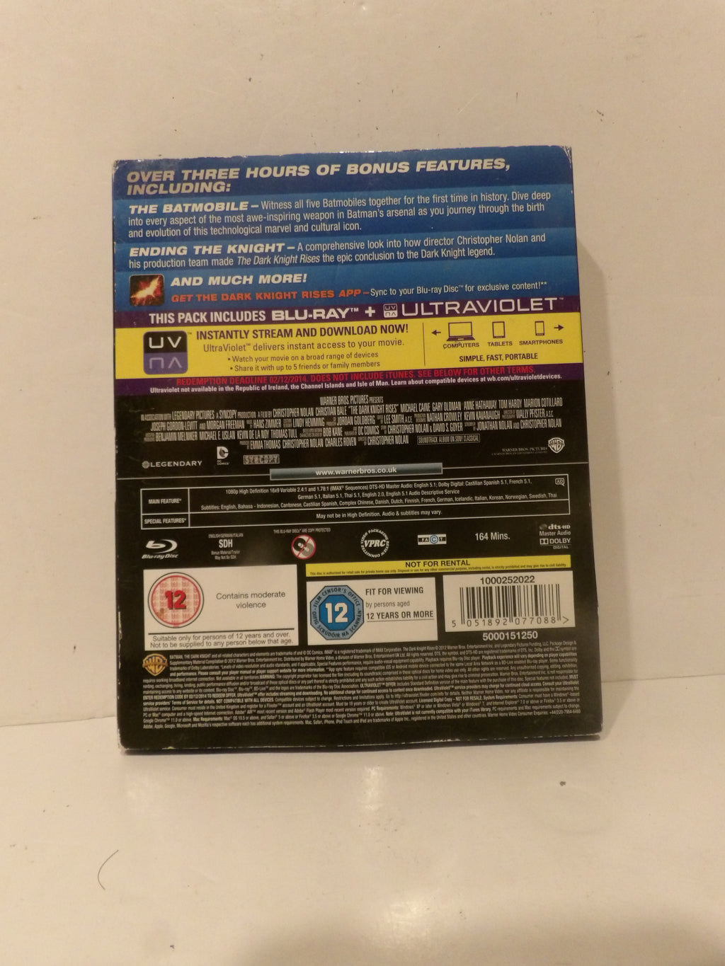 The back cover of a Blu-ray and UltraViolet movie case, photographed on a light off-white surface. The packaging features the title 'The Batman' and various rating logos including a 12 rating.