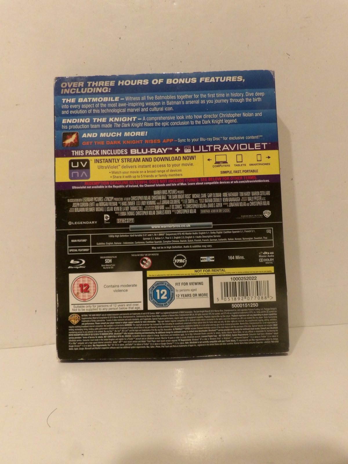 The back cover of a Blu-ray and UltraViolet movie case, photographed on a light off-white surface. The packaging features the title 'The Batman' and various rating logos including a 12 rating.