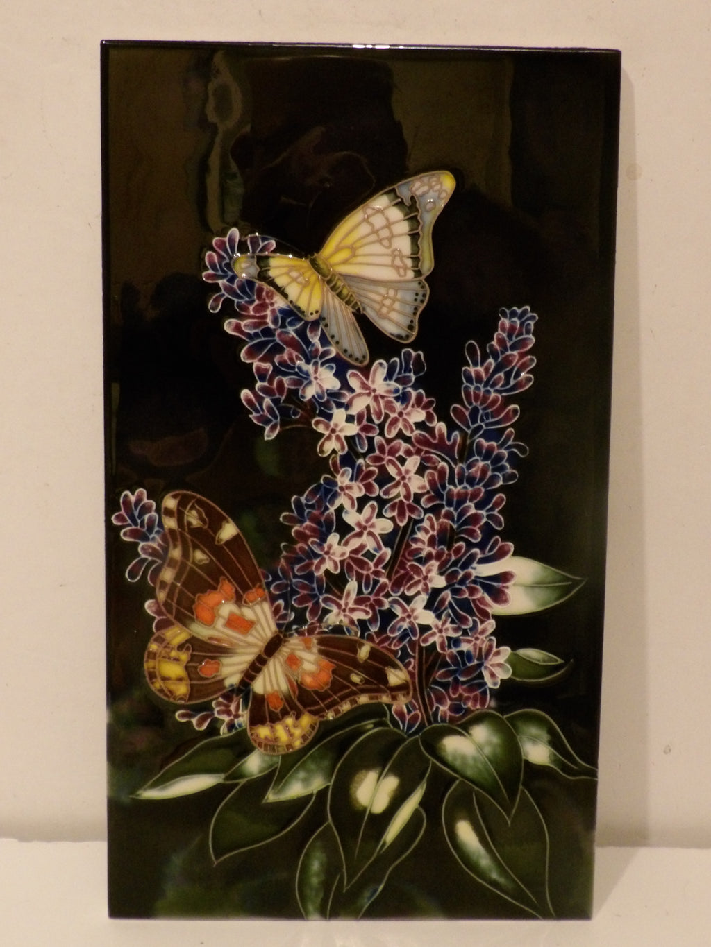 A rectangular glossy black decorative tile featuring a detailed illustration of two butterflies perched on purple and white hyacinth flower clusters with green leaves.
