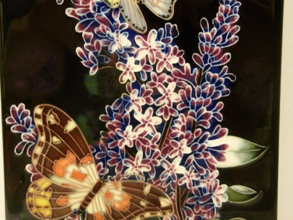 A close-up of a decorative floral and butterfly design on a dark background, featuring purple and white blossoms with brown, orange, and cream butterflies.