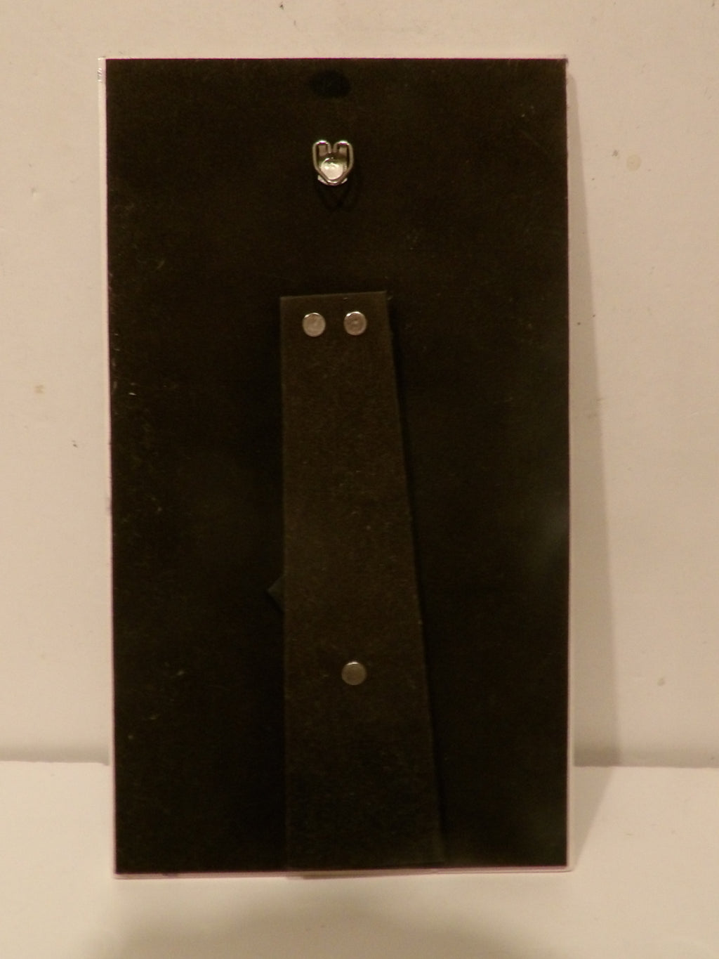 A black rectangular wall hook or pegboard with a vertical mounting strip and silver metal hardware, shown against a plain off-white background.