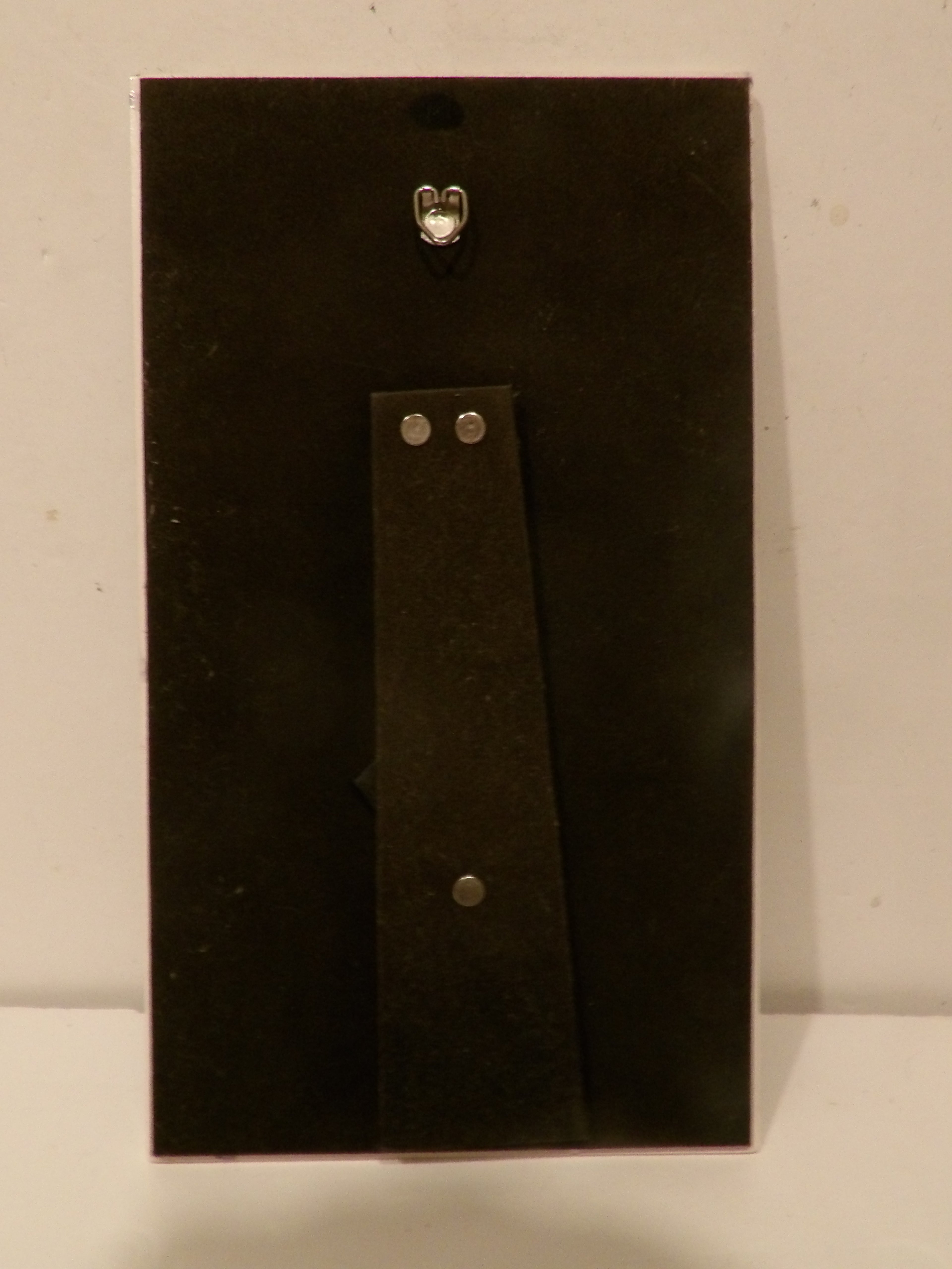 A black rectangular wall hook or pegboard with a vertical mounting strip and silver metal hardware, shown against a plain off-white background.
