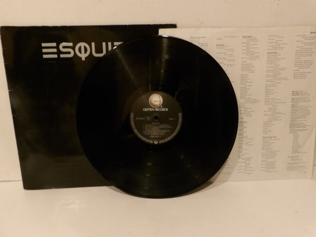 A black vinyl record partially pulled from its black sleeve, with the printed inner label reading 'Geffen Records' visible. The sleeve has large white 'ESQU.