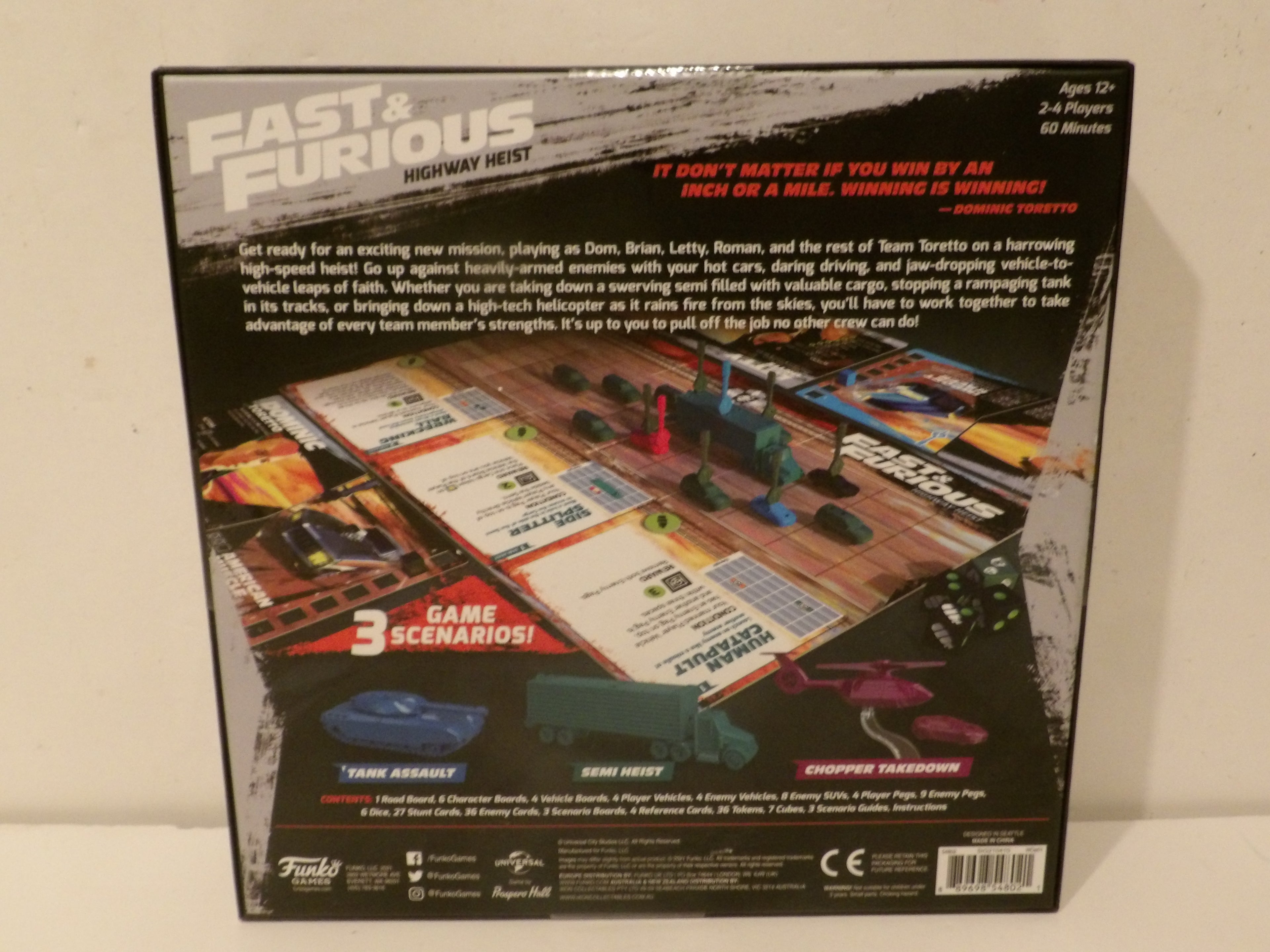 Back of the Fast & Furious Highway Heist board game box, showing the game board layout, miniatures, vehicles, and feature callouts on a white background.