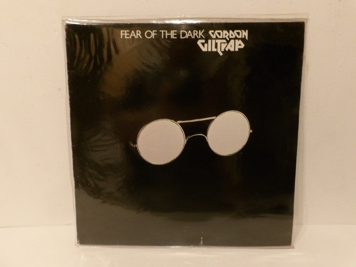 Fear of the Dark (Grittap) album cover by Gordon Giltrap, featuring a black background with a pair of round silver-framed sunglasses in the center, photographed inside a clear plastic sleeve.