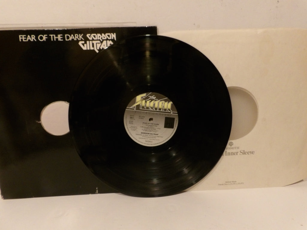 A black vinyl record partially covering its black outer sleeve and cream-colored inner sleeve, with the title 'FEAR OF THE DARK' and artist 'Gibson' visible on the cover.