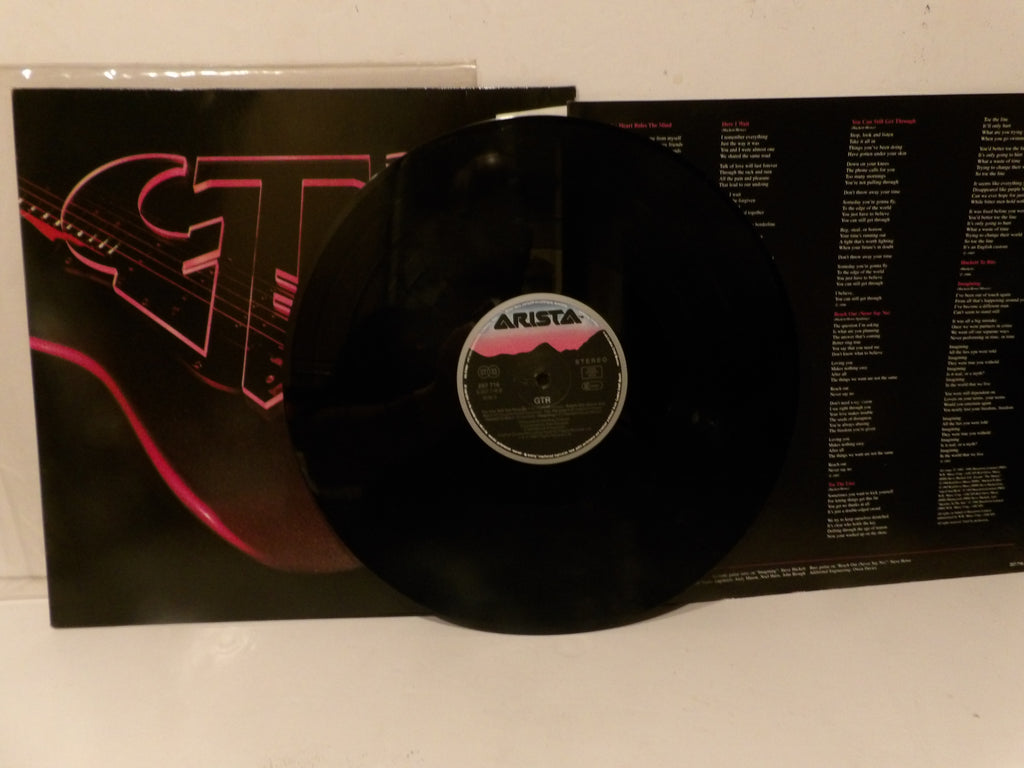 A black vinyl record partially pulled from its sleeve, with the album cover and printed inner sleeve visible behind it on a white surface.