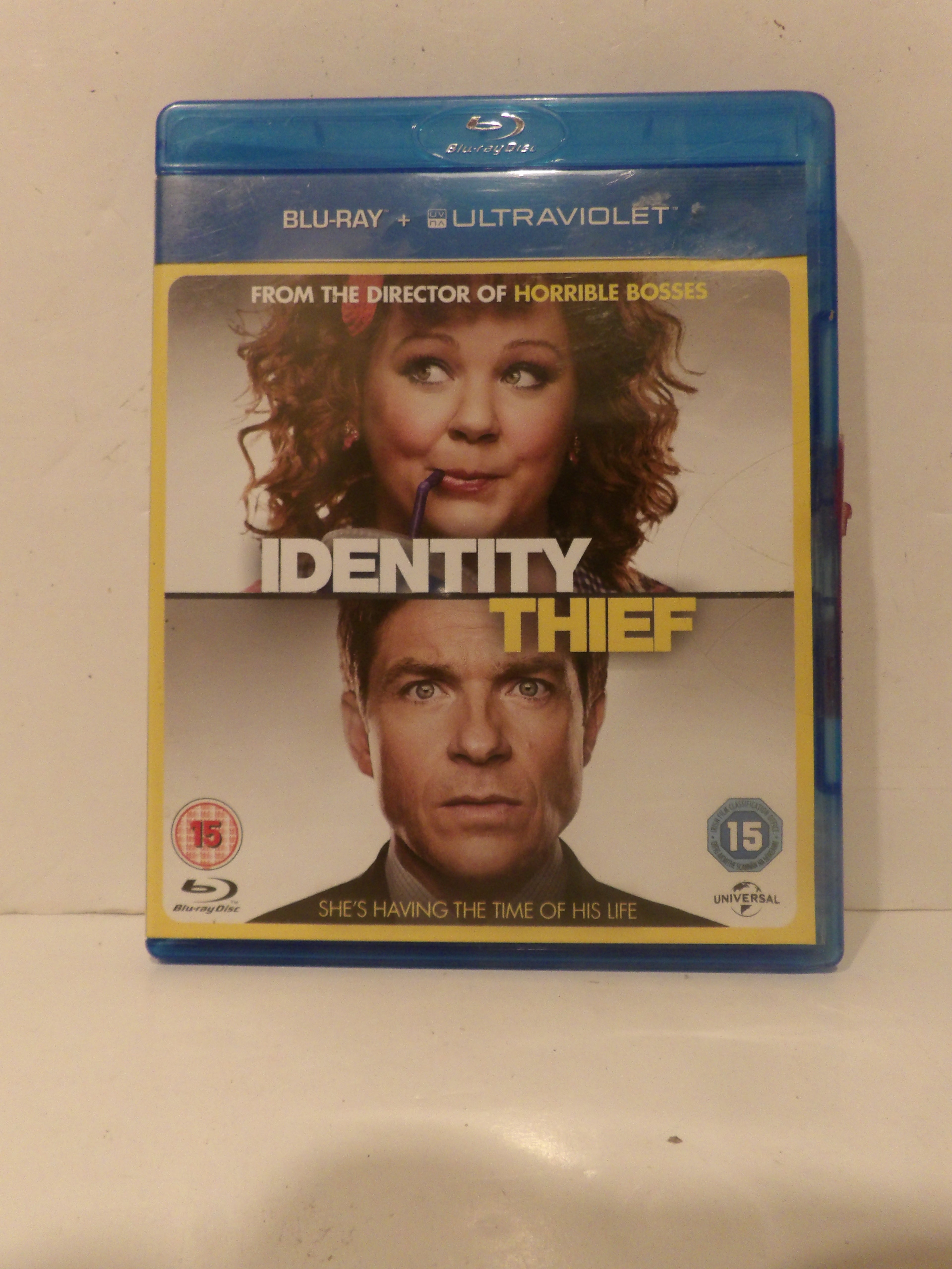 A Blu-ray case for the movie 'Identity Thief' in blue plastic packaging, photographed standing upright against a light beige wall and white surface.