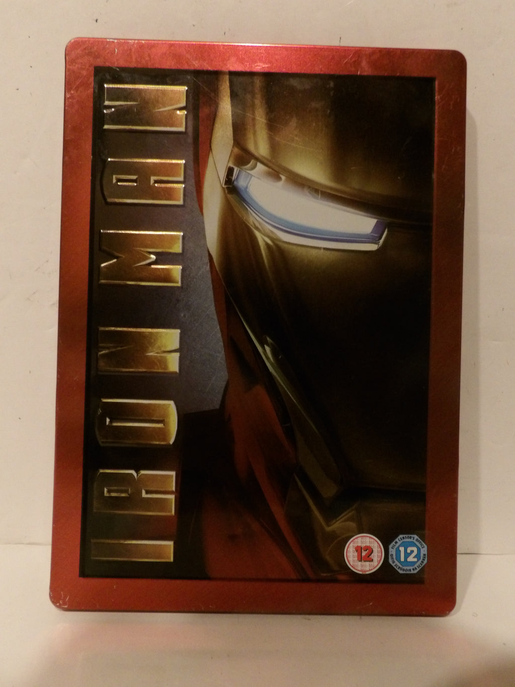 Iron Man steelbook case with a metallic red border and artwork of Iron Man's helmet and the vertical 'IRON MAN' title, photographed against a light background.