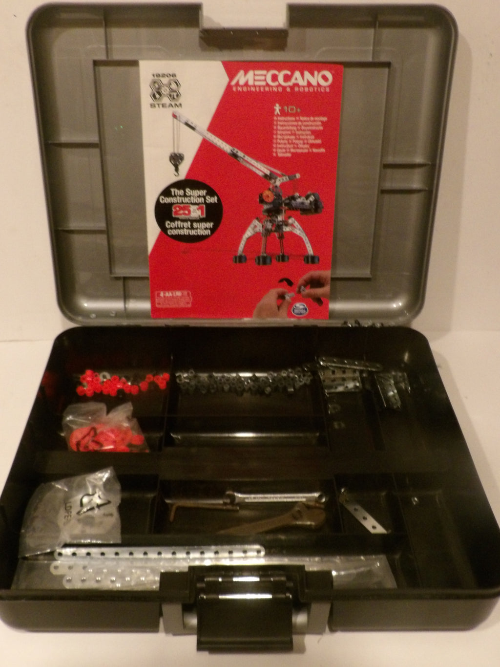 Open Meccano Engineering & Construction Super Construction Kit in a gray plastic storage case, showing various metal parts, red plastic connectors, and the product insert card.