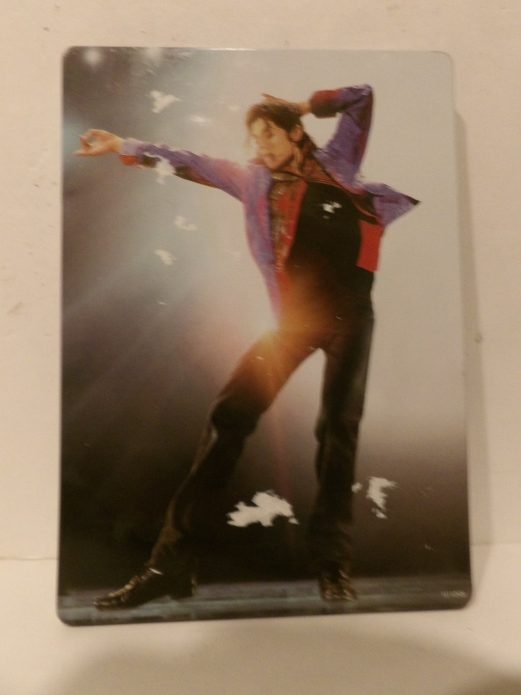 A rectangular printed card or photo featuring a performer in a purple and red jacket posing on stage, photographed against a plain light background.