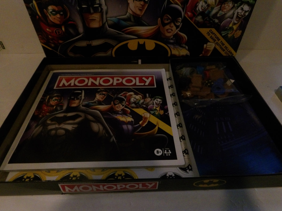 A Batman-themed Monopoly board game set displayed open, showing the game board, play money, and a card deck inside a box with Batman and Robin artwork on the packaging.
