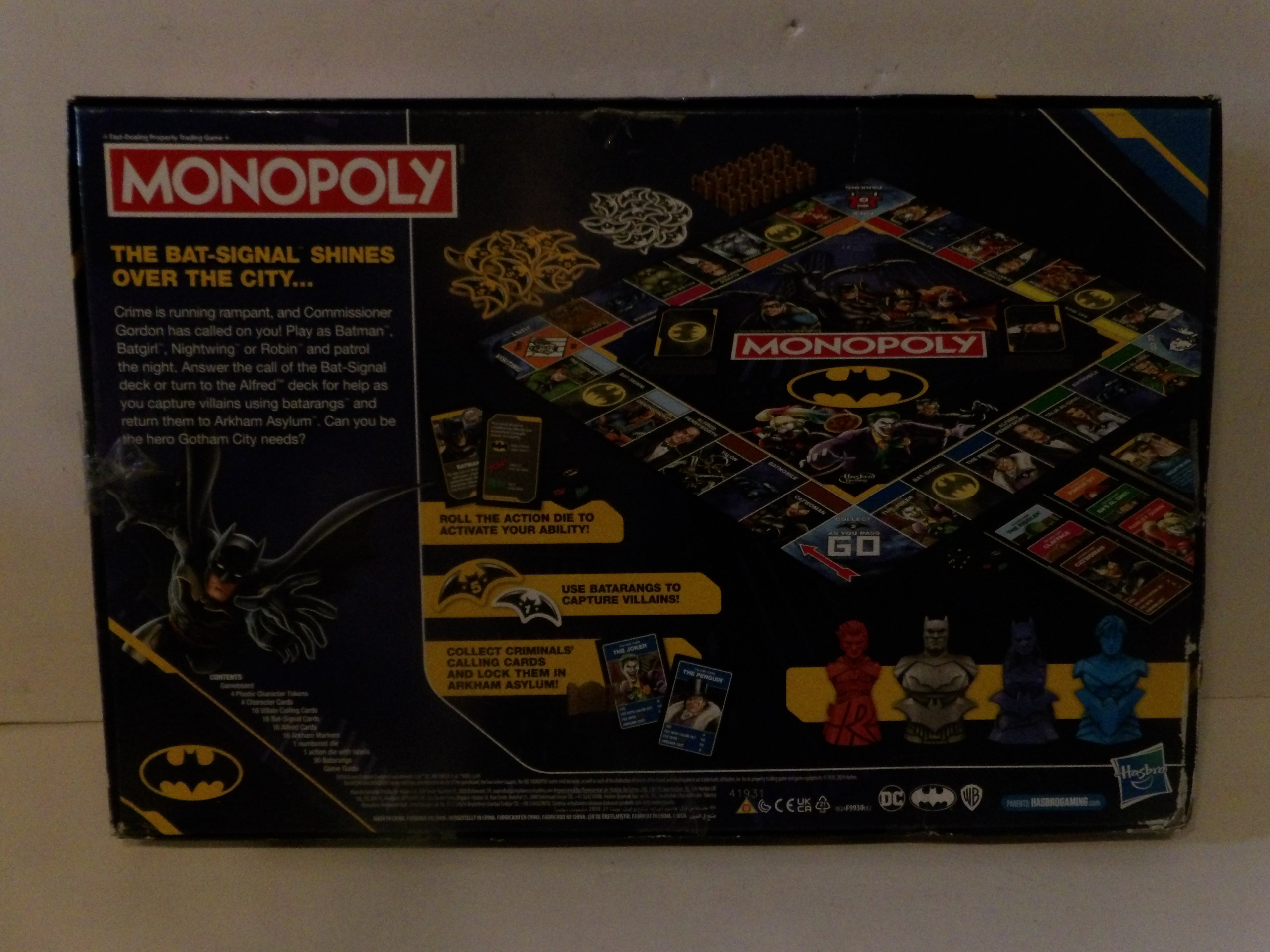 The back of a vintage Monopoly Batman board game box, showing the board layout, game pieces, and Batman-themed graphics on a light-colored surface.