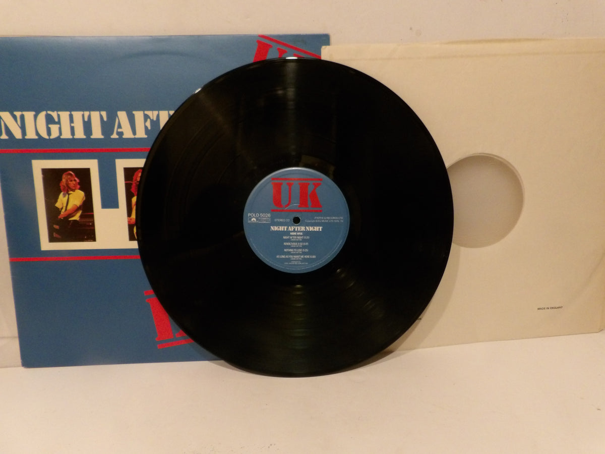 A black vinyl record with a blue and red UK label in the center, displayed in front of its blue and white album cover.