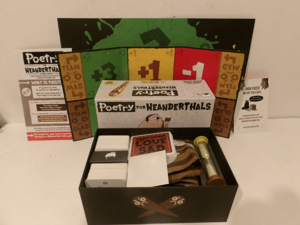 The 'Poetry for Neanderthalts' board game set displayed on a white surface, showing the main game box, an open black storage box with cards, a board, and various illustrated tokens and accessories.
