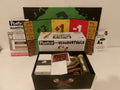 The 'Poetry for Neanderthalts' board game set displayed on a white surface, showing the main game box, an open black storage box with cards, a board, and various illustrated tokens and accessories.