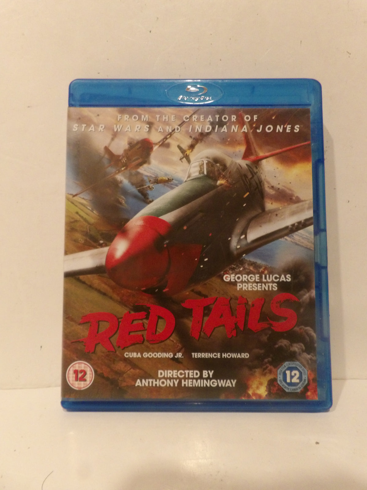 A Blu-ray case for the movie 'Red Tails' standing upright against a plain off-white background. The cover art features a red and gray fighter plane in flight with dramatic explosions, and the title 'RED TAILS' is printed in large red letters.