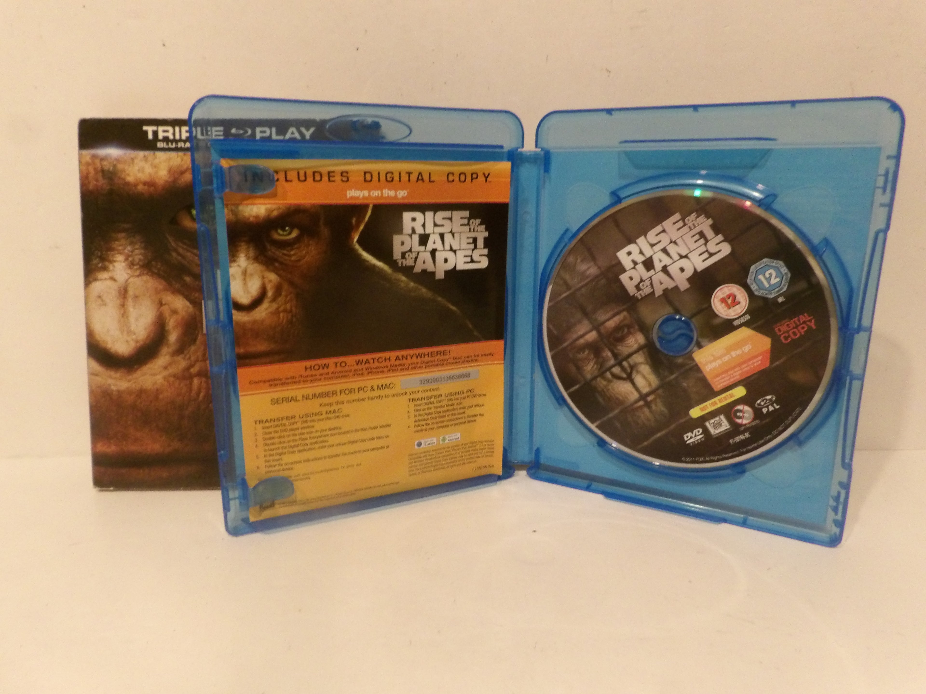 A physical copy of the movie 'Rise of the Planet of the Apes' displayed in a blue plastic Blu-ray case, showing the front cover, back insert, and the disc inside. The Blu-ray case is standing next to its outer sleeve on a plain white surface.
