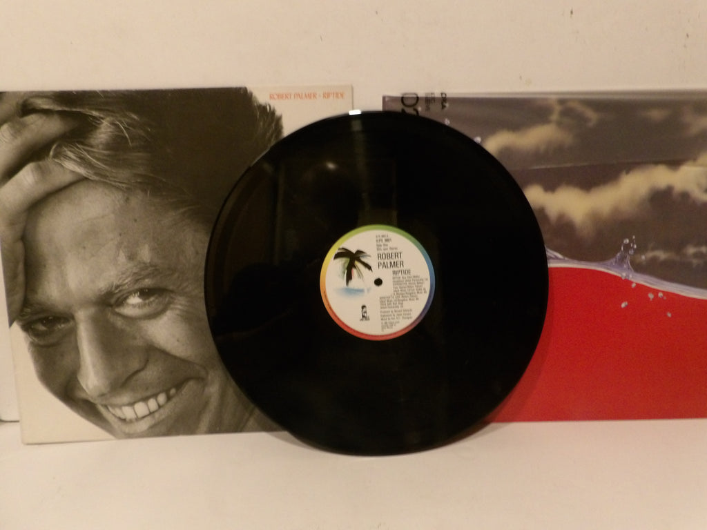 A black vinyl record with a colorful palm tree label in the center, displayed in front of its album cover. The album cover features a black-and-white close-up portrait of a smiling man on the left and a red and gray scenic design on the right.