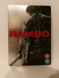 Rambo 1 film steelbook case featuring a black and white graphic of a man in the rain with bold red 'RAMBO' title text and 'STALLONE RAMBO' lettering, photographed on a light surface.