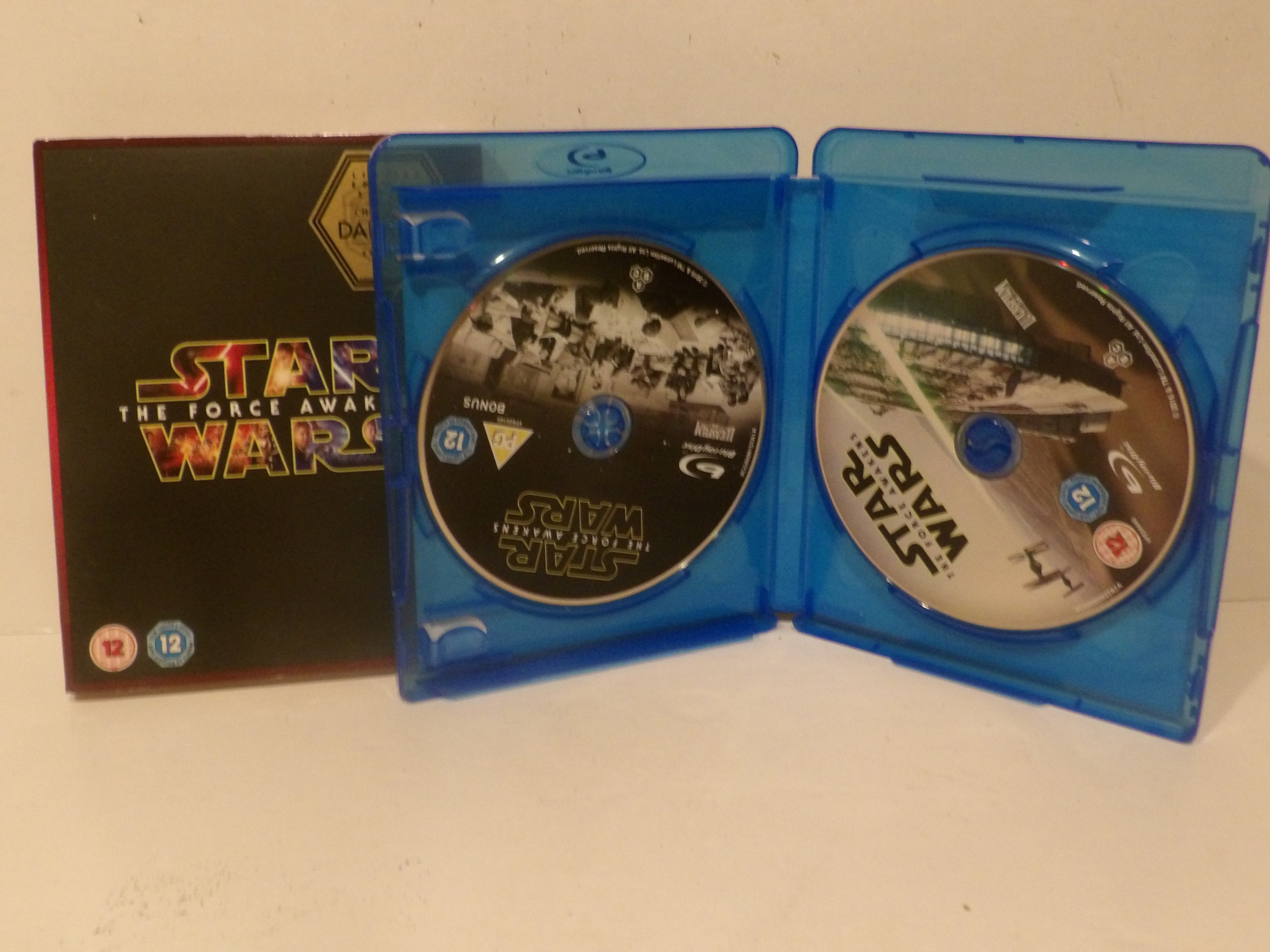 Star Wars: The Force Awakens Blu-ray case shown open with both discs visible, alongside the black outer sleeve on a plain light background.