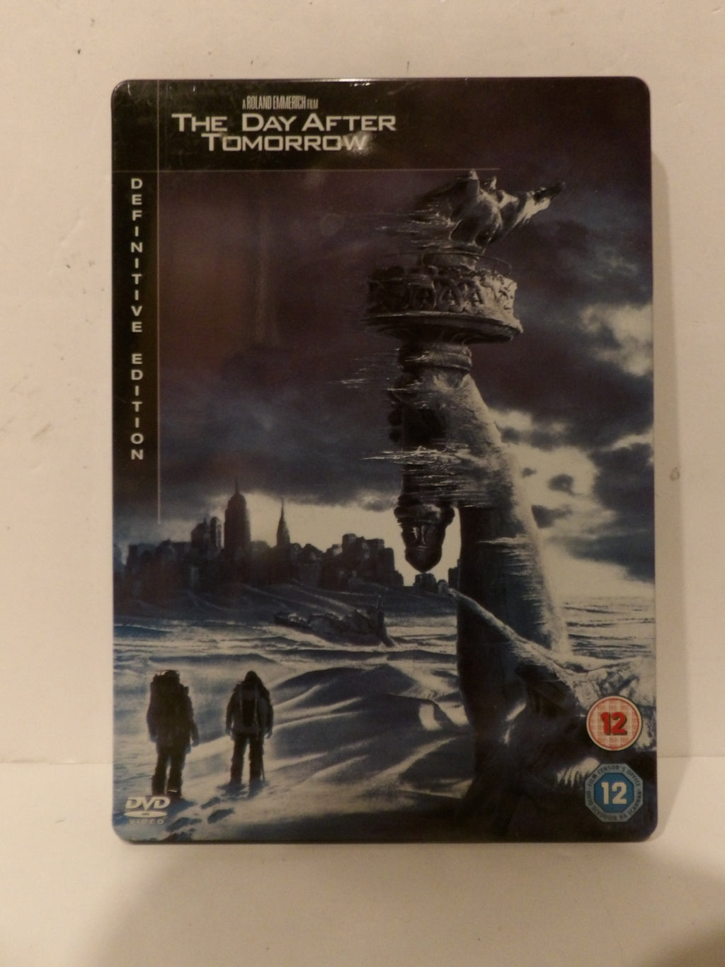 The Day After Tomorrow Definitive Edition DVD steelbook case, featuring a dark, snowy sci-fi cover art with the Statue of Liberty and two figures in a ruined city landscape.