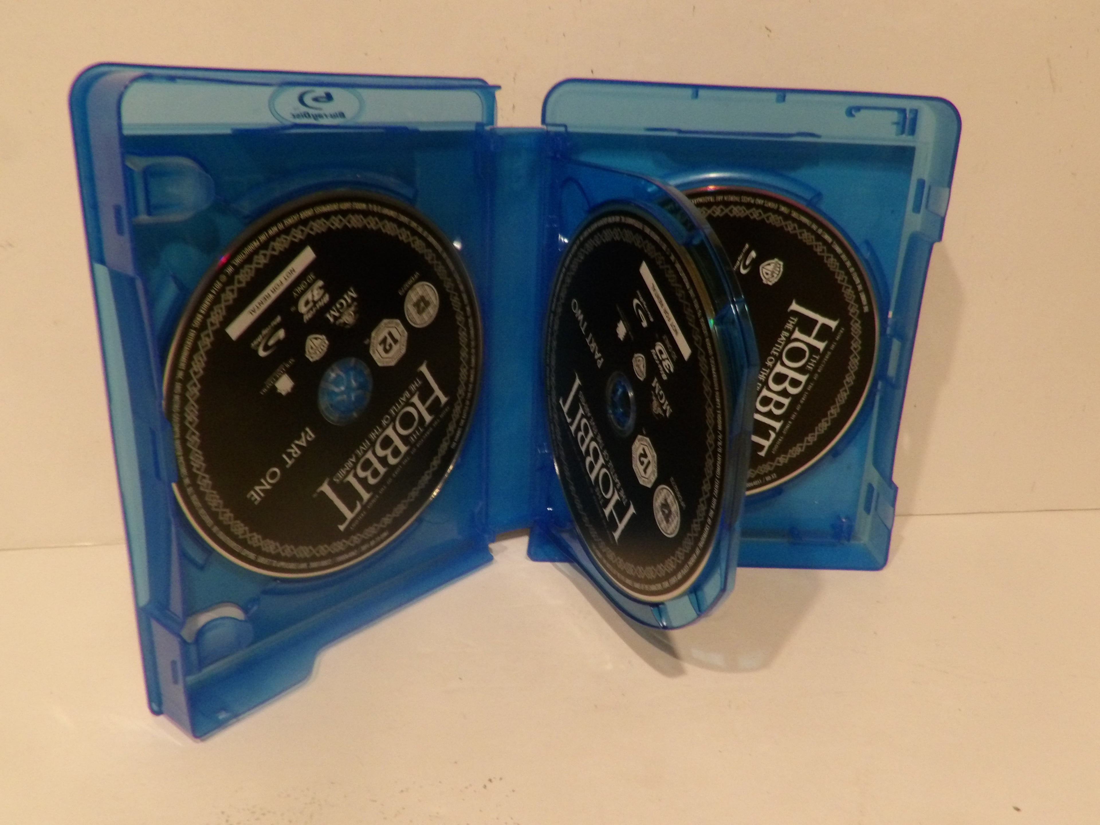 A blue plastic Blu-ray case opened to show two black Hobbit movie discs inside, photographed against a plain light background.