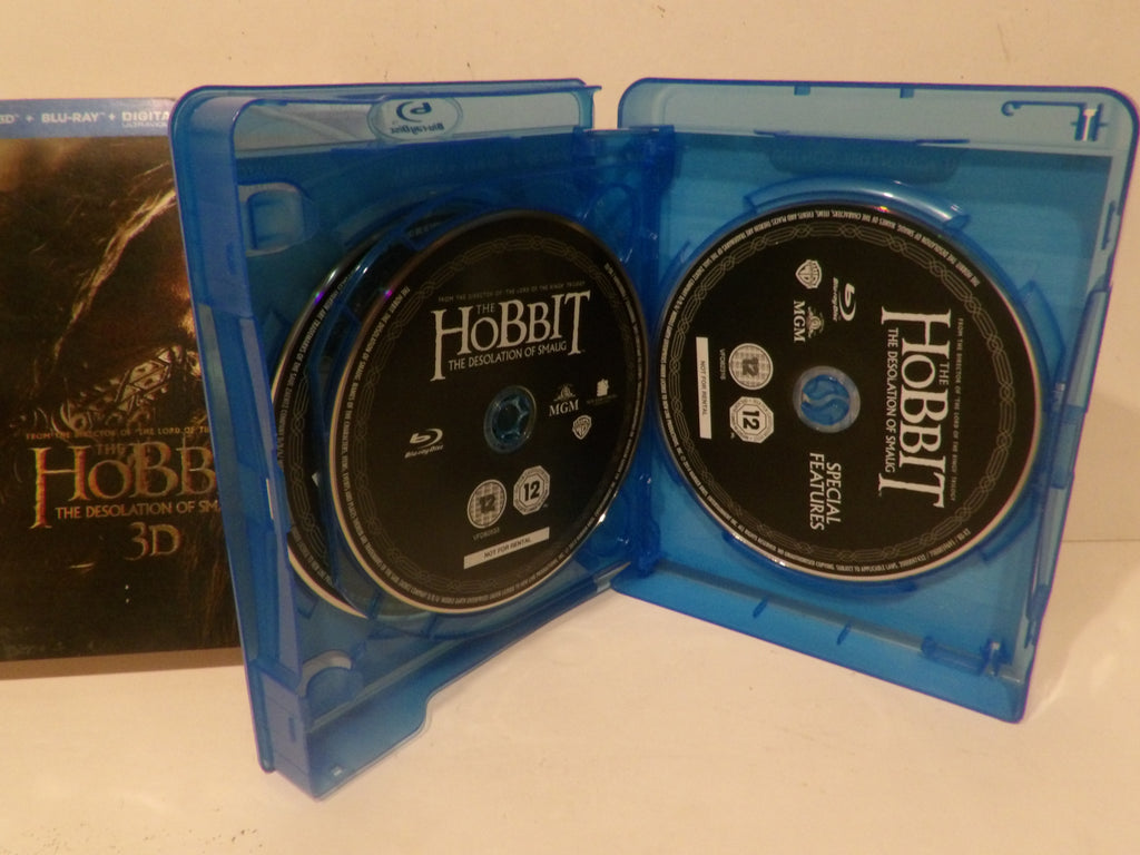 A blue plastic Blu-ray case open to show two discs for The Hobbit: The Desolation of Mordor 3D Blu-ray, with the case standing upright on a white surface and a box partially visible behind it.