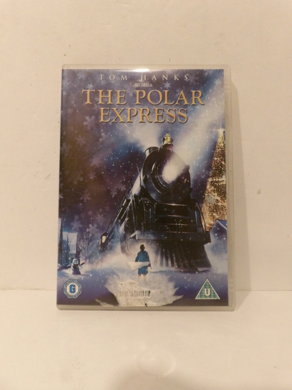 The Polar Express DVD movie case standing upright against a plain off-white wall. The cover shows a dark steam locomotive in snow with the title 'THE POLAR EXPRESS' in gold lettering and 'TOM JANKS' above it.