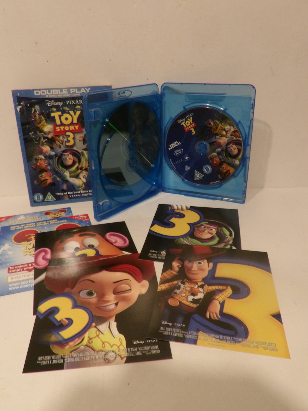 Disney Pixar Toy Story 3 double play Blu-ray set with the blue plastic case open, showing the disc inside, plus several printed character posters and a smaller insert on a plain light background.