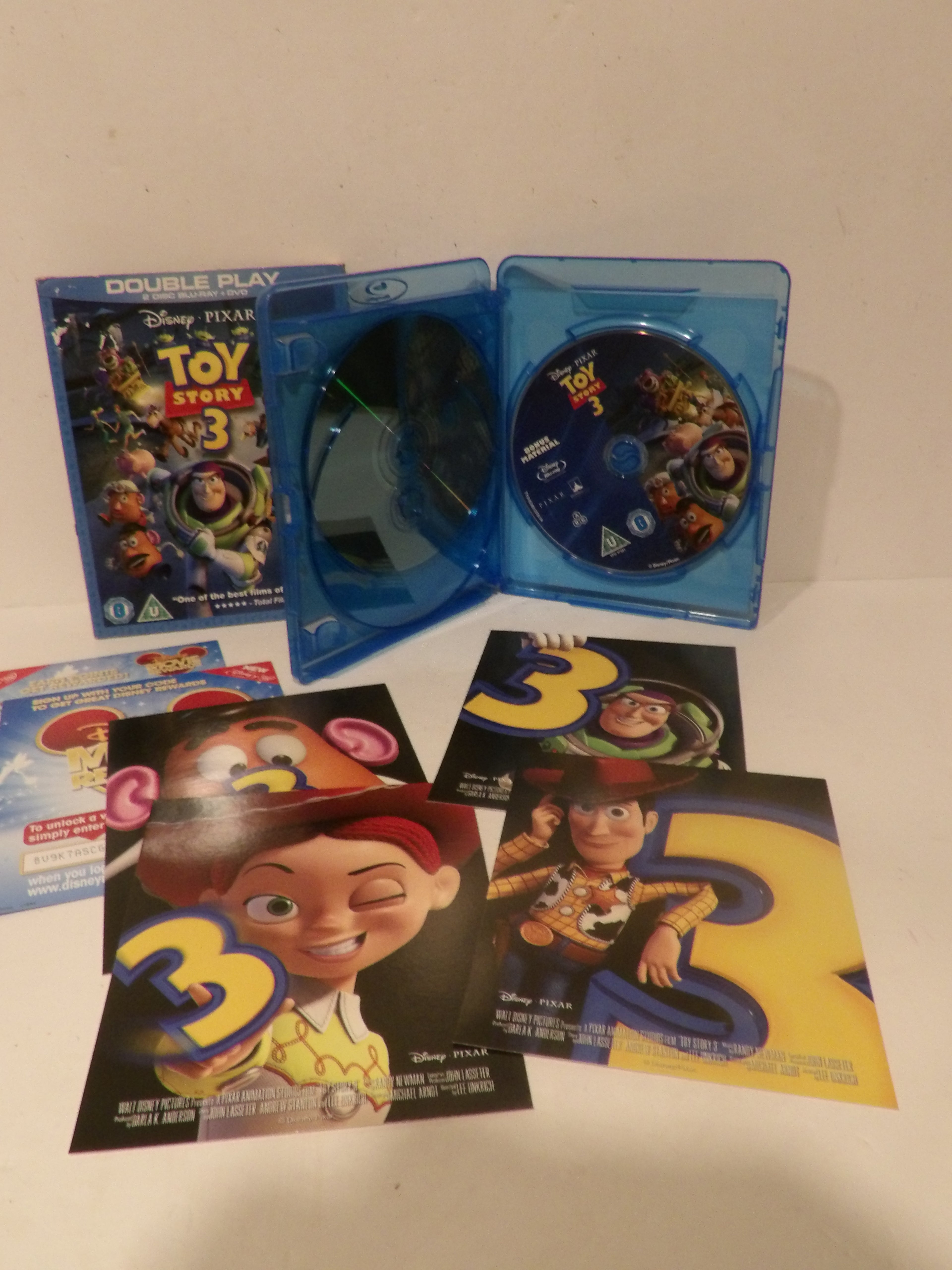 Disney Pixar Toy Story 3 double play Blu-ray set with the blue plastic case open, showing the disc inside, plus several printed character posters and a smaller insert on a plain light background.
