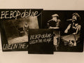 A set of three black square album art prints or sleeves for 'BE BOP deluxe LIVE! IN THE ARAGE', featuring black-and-white photos of a musician performing, displayed against a plain off-white background.
