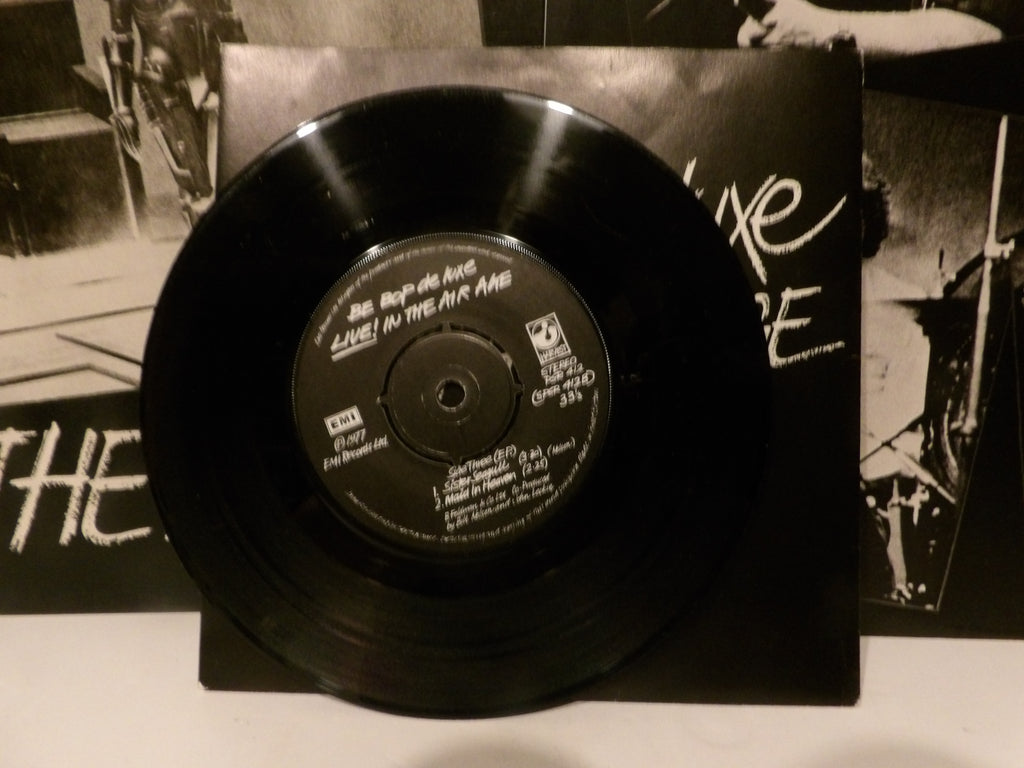 A black vinyl record for Bob Dylan's 'Live in the Air Amb' displayed in front of its black paper sleeve, which features white handwritten text and band photos.