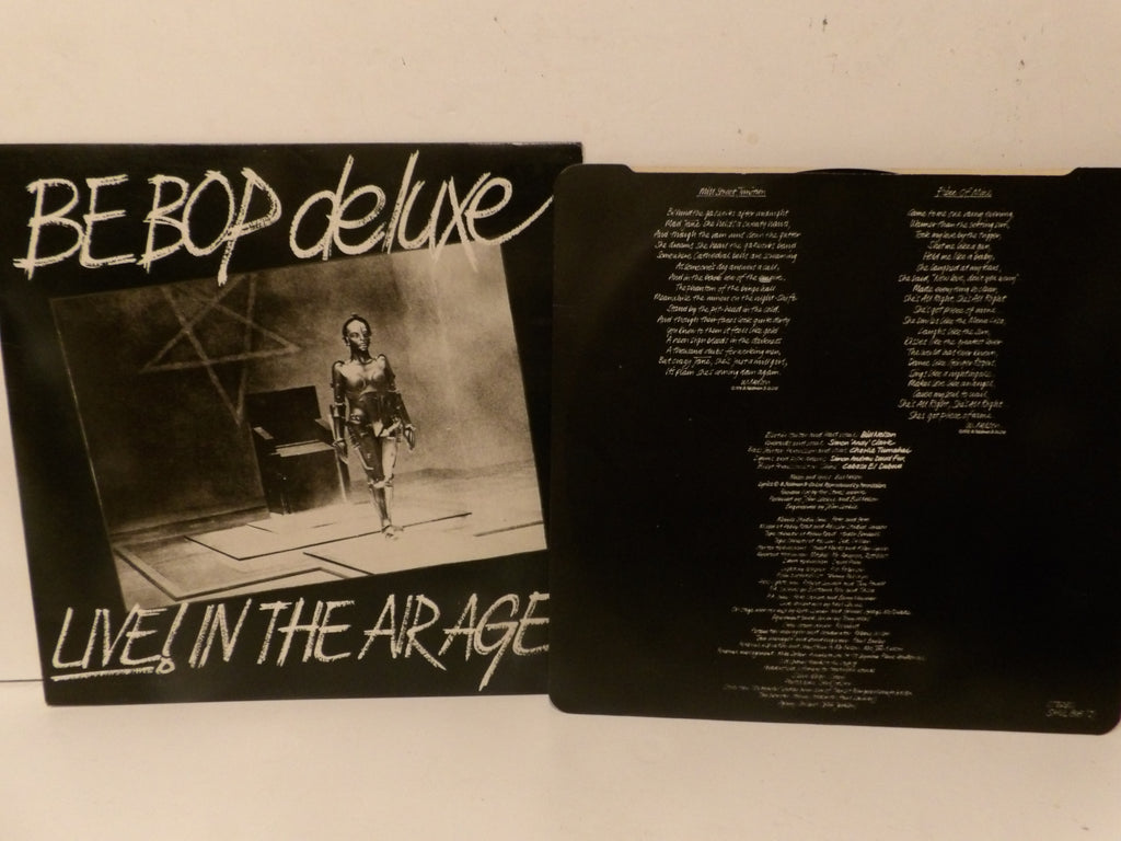 A vinyl record sleeve and its inner printed insert for 'BE BOP deluxe - Live in the Airage' are displayed side-by-side on a light-colored surface.