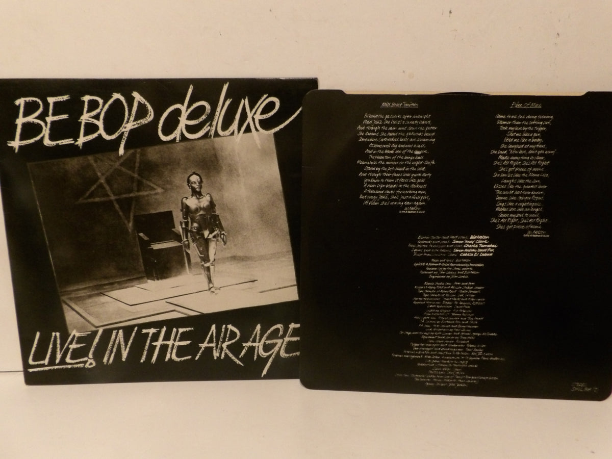 A vinyl record sleeve and its inner printed insert for 'BE BOP deluxe - Live in the Airage' are displayed side-by-side on a light-colored surface.